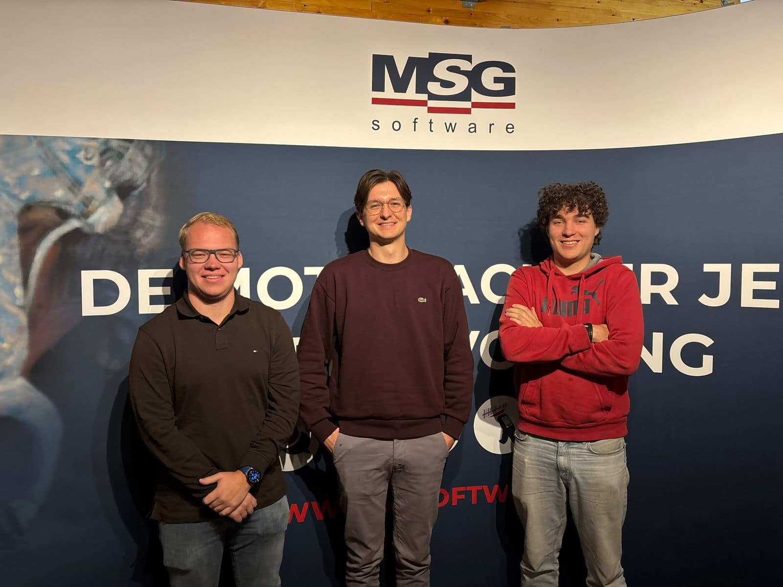 De drie stagiairs Nick, Boyan en Storm naast elkaar voor de banner van MSG software op kantoor